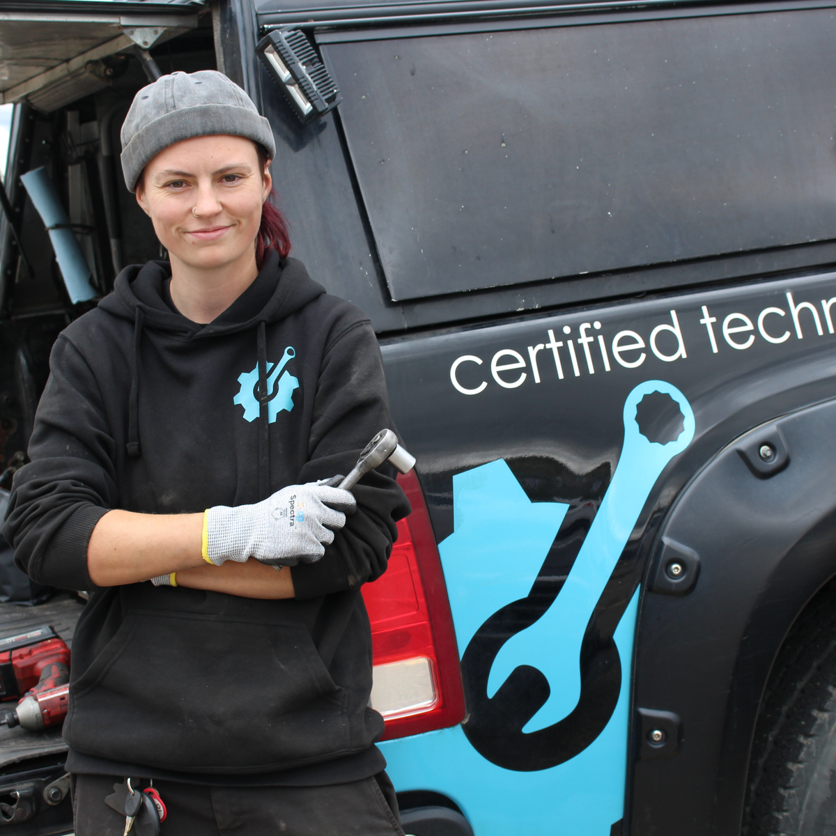 Person wearing Rockette work gloves and holding a ratchet beside a service truck
